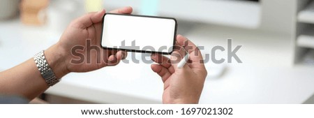 Cropped shot of male entrepreneur using horizontal blank screen smartphone while sitting at minimal office desk
