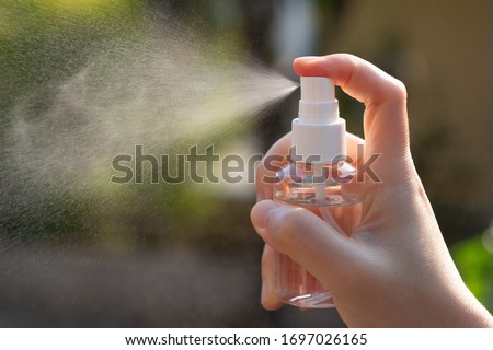 Hand of Asian woman applying the alcohol spray with greenery background. Closed up alcohol spray. Killing the virus. Royalty-Free Stock Photo #1697026165