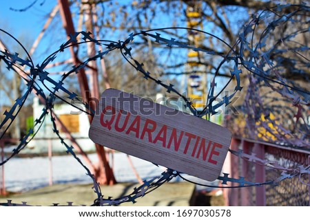 Concept for restricted area on coronavirus global quarantine. View through barbed wire with sign quarantine in entrance at park or square on blurred background