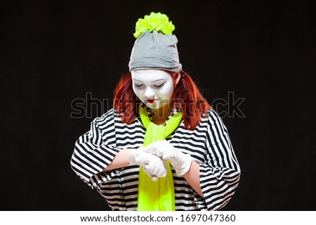 Portrait of female mime artist, isolated on black background. Young woman in striped clothes and bright yellow scarf looking at her watch. Symbol of waiting, time, punctuality