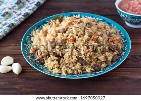 National cuisine - Uzbek pilaf with meat in a plate with a traditional pattern, on a dark wooden table. Dastarkhan. Navruz concept