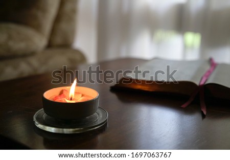 Burning candle on the table with book, curtain and couch at the background