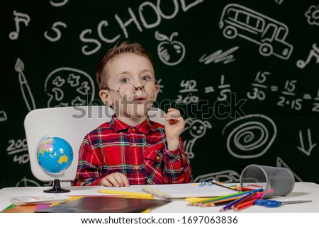 Emotional school boy sitting on the desk with many school supplies. First day of school. Back to school. 