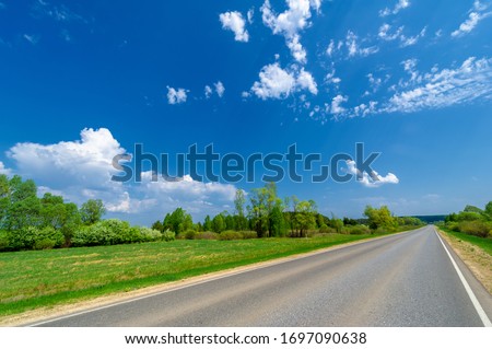 spring photo taken with a wide-angle lens, local highway, bright green trees, clouds in the blue sky