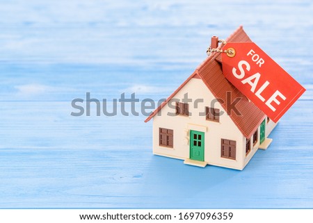 Affordable existing house for sale / reverse mortgage, financial concept : Model home with a tag for sale on wood background, depicts selling asset or changing property to cash for personal expense