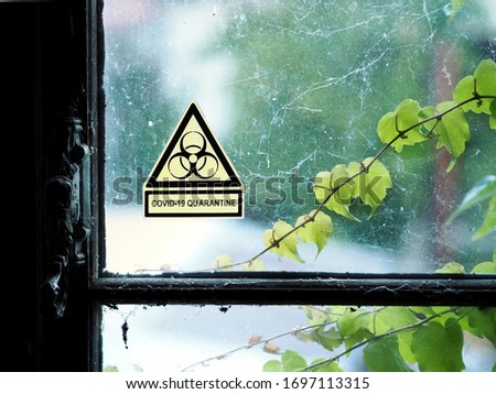 warning sign, biohazard symbol, message COVID-19 Quarantine on old dirty glass window panes covered in cobwebs. Close up view of Dirty old glass windows with window handle with cobweb. view outside