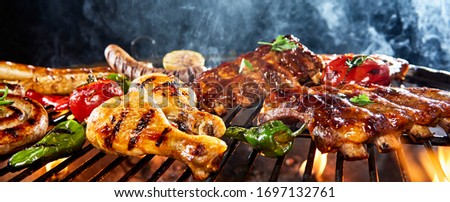 Assorted meat grilling over a BBQ outdoors in a low angle view of chicken legs, pork ribs, sausages and vegetables with rising smoke and copy space in a panorama banner