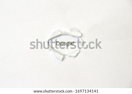 Word danger on white isolated background, the inscription through the wound hole in the paper. Stock photo for web and print with empty space for text and design.