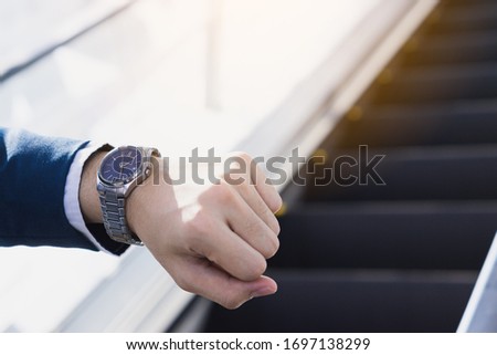 The photo close up of businessman watching his watch in his hand while standing on the escalator. Business and finance concept.