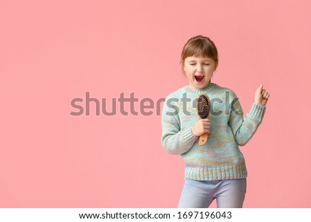 Little girl using hair brush as microphone on color background