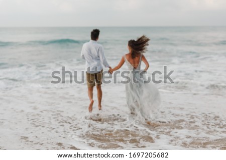 Blurred image of just married wedding couple running into the ocean. Romantic love picture background, wedding by the sea