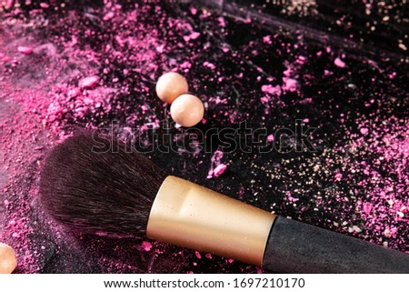 A make-up brush with broken cosmetics and pearls on a black background with a place for text