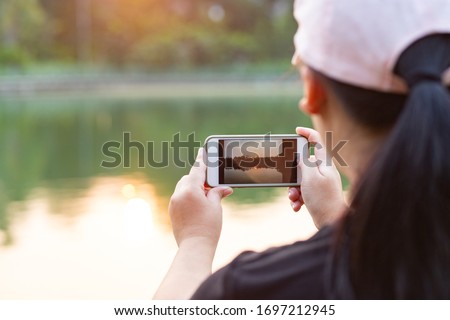 Rear view of woman holding smart phone to take sunset landscape photo in the evening