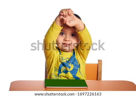 Young child girl is using tablet while sitting at table, hands up, isolated over white background