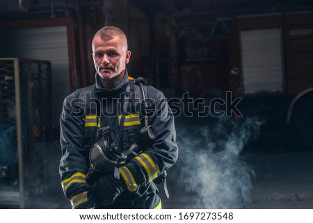Portrait of a fireman wearing firefighter turnouts and helmet. Dark background with smoke and blue light.
