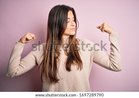 Young beautiful girl wearing casual turtleneck sweater standing over isolated pink background showing arms muscles smiling proud. Fitness concept. Royalty-Free Stock Photo #1697289790