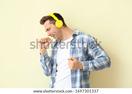 Cool young man dancing and listening to music against color background