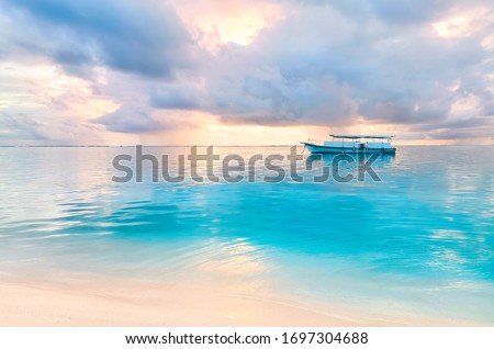 Beautiful natural landscape of coast of a tropical beach with a boat in ocean at sunset with beautiful pink clouds.