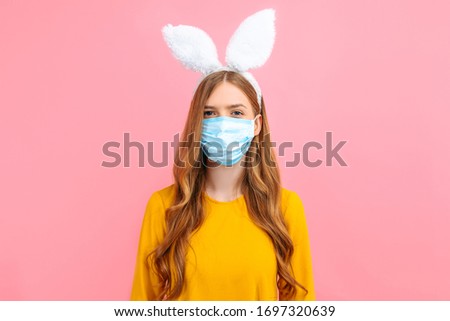 A young girl in the ears of an Easter Bunny, wearing a medical mask on her face against viral diseases, on an isolated pink background