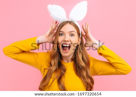 Shocked excited happy young woman in Easter Bunny ears isolated on pink background.