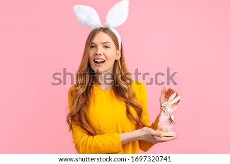 happy Easter. Happy young woman in Easter Bunny ears, holding a wooden rabbit toy, on an isolated pink background