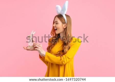 happy Easter. Happy young woman in Easter Bunny ears, holding a wooden rabbit toy, on an isolated pink background