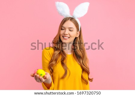 The concept of a happy Easter. A happy young girl with rabbit ears holds colorful Easter eggs, on a pink background.
