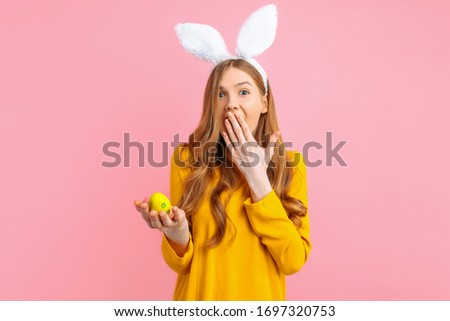 The concept of a happy Easter. Happy, surprised, shocked girl with rabbit ears holding colorful Easter eggs, on a pink background.