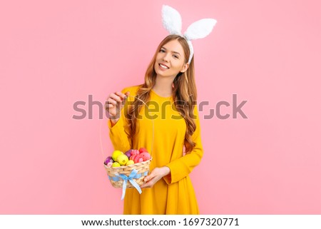 Happy Easter. A beautiful happy young woman wears rabbit ears on Easter day and holds a basket of Easter eggs, on an isolated pink background. Beautiful girl is getting ready for Easter