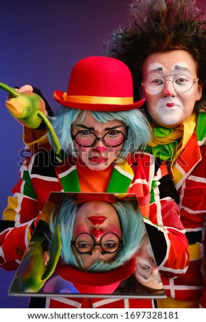 two clowns a man and a woman with bright makeup in colored costumes say they look at their reflection in the mirror. April Fools Day concept. Birthday for kids