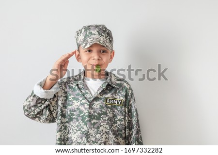Little saluting African-American soldier with whistle on light background