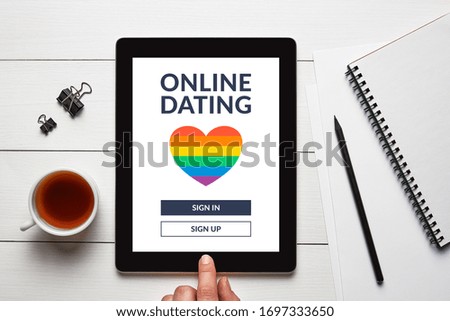 LGBT dating app concept on tablet screen with office objects on white wooden table. Gay online dating. Top view