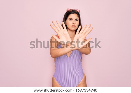 Young beautiful fashion girl wearing swimwear swimsuit and sunglasses over pink background Rejection expression crossing arms and palms doing negative sign, angry face