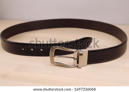 a stylish belt made of smooth black leather and steel fittings lies on a light, wooden background. Expensive gift option for men, women, premium leather, chic performance, handmade, exclusive,
