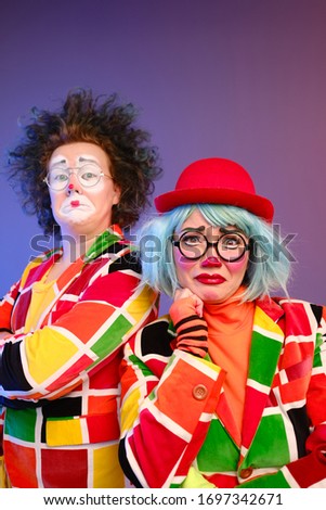 Two clowns a man and a woman with makeup in bright colored costumes are fooling around and showing a presentation using various accessories. April Fools Day concept. Birthday for kids