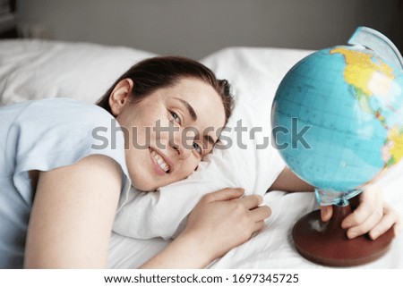 Beautiful woman dreaming about vacation. Girl holds in hand a small globe and laying in the bed.