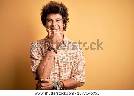Young handsome man on vacation wearing summer shirt over isolated yellow background looking confident at the camera smiling with crossed arms and hand raised on chin. Thinking positive.