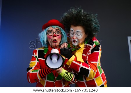Two clowns a man and a woman with bright makeup in colored costumes speak in a megaphone to make an announcement. April Fools Day concept. Birthday for kids