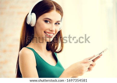 Happy attractive woman listening cellphone with headphones at home, indoor. Caucasian beautiful brunette model in technology and leisure concept picture.