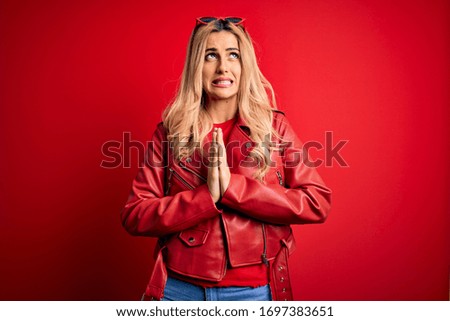 Young beautiful blonde woman wearing casual jacket standing over isolated red background begging and praying with hands together with hope expression on face very emotional and worried. Begging.