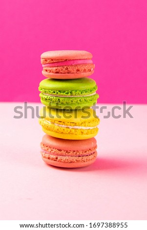 Multi-colored macaroons stand in a pile on a pink table. Close-up