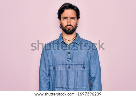 Young handsome hispanic bohemian man wearing hippie style over pink background depressed and worry for distress, crying angry and afraid. Sad expression.