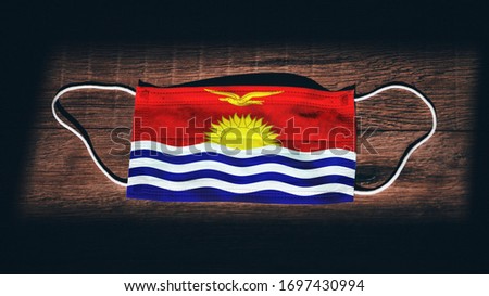 Kiribati National Flag at medical, surgical, protection mask on black wooden background. Coronavirus Covid–19, Prevent infection, illness or flu. State of Emergency, Lockdown