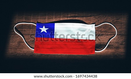 Chile National Flag at medical, surgical, protection mask on black wooden background. Coronavirus Covid–19, Prevent infection, illness or flu concept photo. State of Emergency, Lockdown