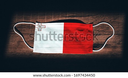Malta National Flag at medical, surgical, protection mask on black wooden background. Coronavirus Covid–19, Prevent infection, illness or flu. State of Emergency, Lockdown