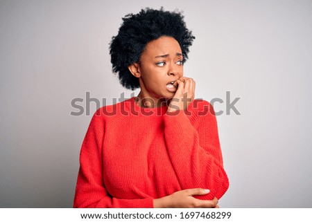 Young beautiful African American afro woman with curly hair wearing red casual sweater looking stressed and nervous with hands on mouth biting nails. Anxiety problem.