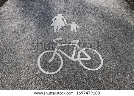 The old pedestrian traffic sign marking painted on asphalt on the road surface a white bicycle and a child. Walking woman and a kid warning pavement sign