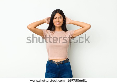 young pretty latin woman feeling stressed, worried, anxious or scared, with hands on head, panicking at mistake against flat wall