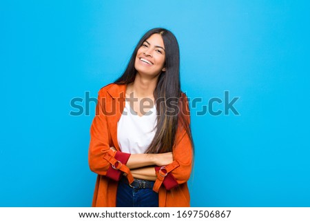 young pretty latin woman laughing happily with arms crossed, with a relaxed, positive and satisfied pose against flat wall Royalty-Free Stock Photo #1697506867