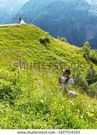 Photographer, high in the mountains, on a mountain slope, among green grass and flowers, conducts a wedding photo shoot